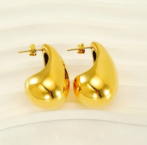 Macro detail of polished gold teardrop earrings on a white textured stand