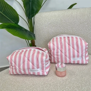 Detail of quilted pink and white striped makeup bags in two sizes on a beige sofa