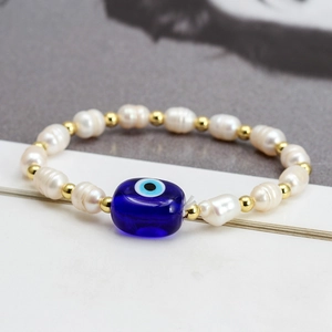 Detail of baroque pearls and evil eye charm on a gold-beaded elastic bracelet
