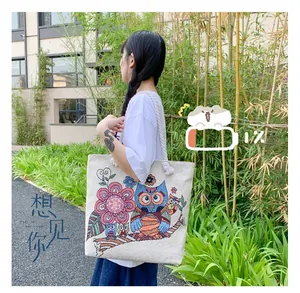 Outdoor shot of a large canvas tote bag with colorful owl embroidery and rope handles