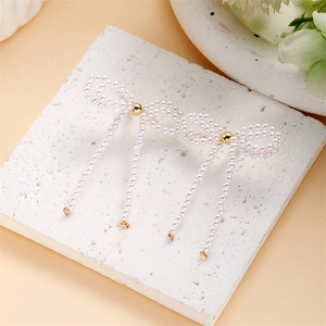 Detailed view of handmade white faux pearl bow earrings with gold metal beads