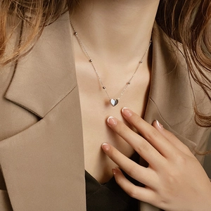Detailed view of a silver heart pendant necklace with beaded chain worn by a model