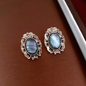 Close-up of vintage oval iridescent teal resin earrings with ornate metal frames