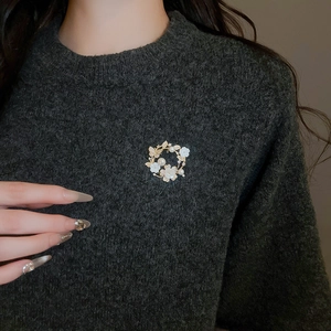 Detailed close-up of a gold floral wreath brooch with pearls on a grey sweater