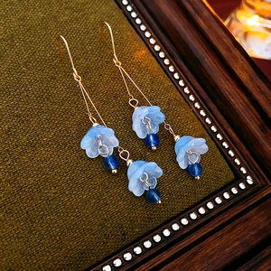 Close-up of elegant long tassel earrings with blue flower petals and golden hooks