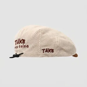 Detail van de crème corduroy baret met borduursel aan de zijkant en trekkoord