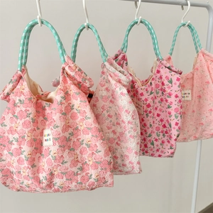 Quilted floral handbags in pink and cream with green rope handles hanging on white rack