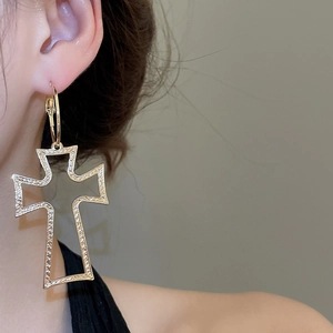 Close-up of a large gold hollow cross pendant earring with textured metallic finish