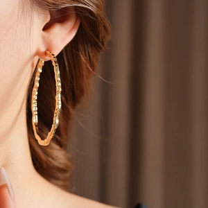 Gros plan de grandes boucles d'oreilles créoles dorées avec texture martelée irrégulière