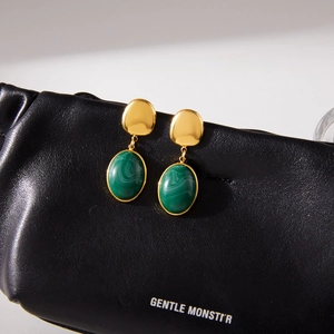 Close-up of gold titanium steel earrings with green resin pendants on a black bag