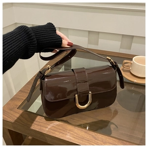 Detailed shot of coffee brown patent leather bag with gold horseshoe hardware on a table