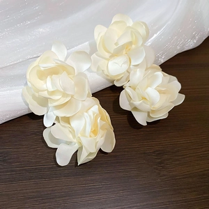Détail macro de boucles d'oreilles fleurs en satin crème avec pétales superposés