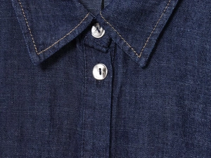 Dettaglio del colletto della camicia di jeans blu scuro con bottoni argento e cuciture