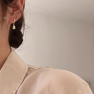 Close-up of elegant 18K gold drop pearl earrings worn by a model in soft lighting