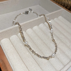 Détail d'une chaîne à maillons argentés avec perles blanches sur boîte à bijoux beige