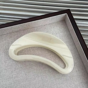 Detail of minimalist moon-shaped hair claw in ivory marble acetate on a wooden tray