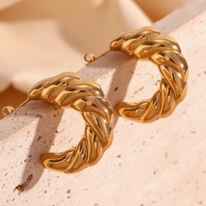 Macro detail of 18K gold plated twisted horn crescent earrings on a stone surface