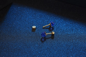Macro detail of square blue crystal stud earrings with gold plated backings on navy texture