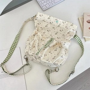 Floral canvas crossbody bag with green checkered strap and drawstring closure details