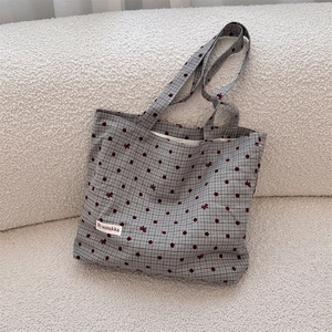 Detailed view of canvas tote bag with red polka dots and brand woven label on white texture