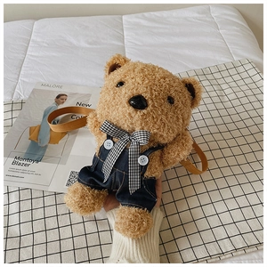 Close-up of cute teddy bear plush bag with denim overalls and checkered bow decoration