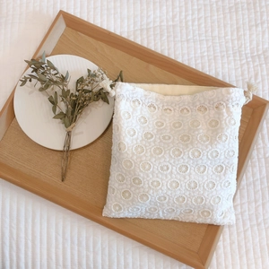 Elegant white lace floral embroidery drawstring storage pouch on a rustic wooden tray