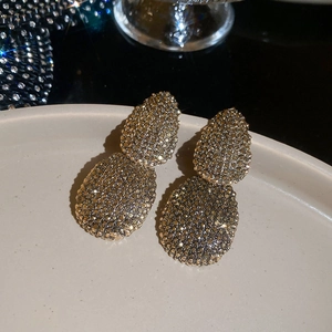 Macro view of vintage gold oval earrings with champagne crystals on a white ceramic plate