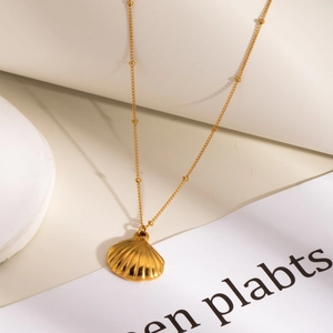 Detail of a golden seashell pendant on a satellite chain over a cream geometric background