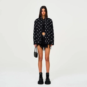 Detail of black cotton shirt with all-over white cross prints and distressed denim shorts
