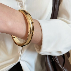 Gros plan d'un large bracelet jonc doré poli à effet miroir porté sur un poignet féminin