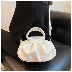 Close-up of white ruched cloud bag with handle and strap on a black leather sofa
