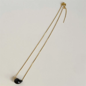 Detail of a minimalist gold necklace featuring a glossy black water drop pendant