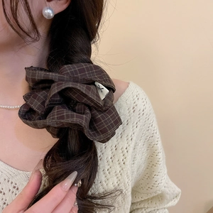 Detail of a dark brown checkered scrunchie worn on a low ponytail with knitwear