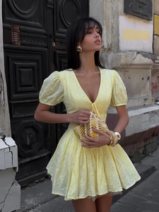 Detail of yellow eyelet mini dress with puff sleeves and deep V-neck in outdoor setting