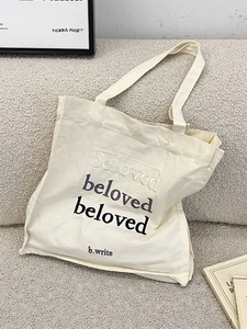Minimalist beige canvas tote bag with beloved embroidery on a modern gray sofa