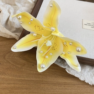 Gros plan d'une élégante pince à cheveux lys en tissu jaune ornée de perles blanches