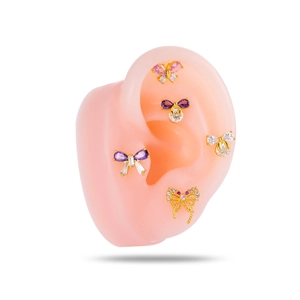 Five bow-shaped gold stud earrings with purple and pink cubic zirconia on a silicone ear model