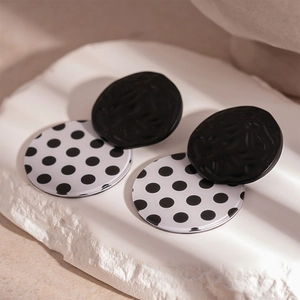 Macro detail of retro black and white polka dot acrylic round stud earrings on stone base
