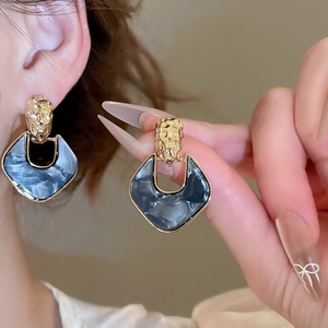 Macro detail of dark blue resin and gold hammered metal earrings worn on ear