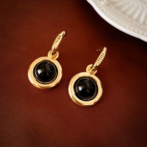 Macro shot of gold geometric earrings with black enamel inlay and engraved logo detail