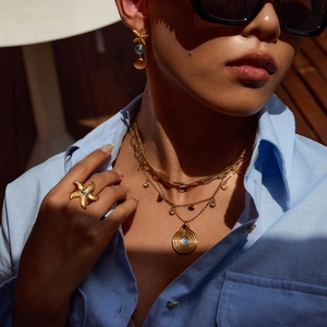 Close-up of golden starfish earrings with blue resin stones and layered necklaces on model