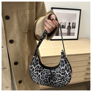 Detailed view of stylish leopard print crescent bag held by a model in a cozy setting