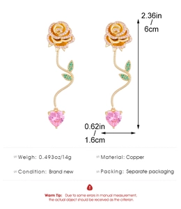 Makroaufnahme goldener Rosenohrringe mit rosa Herzsteinen und grünen Blättern