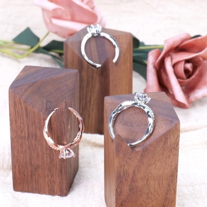 Three diamond rings on walnut wood cone stands with a soft pink rose background