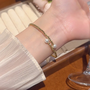 Detail of beaded gold bracelet with two white pearls on a wrist with chiffon sleeve