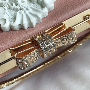 Detail of pink leather evening bag with golden hardware and rhinestone bow clasp
