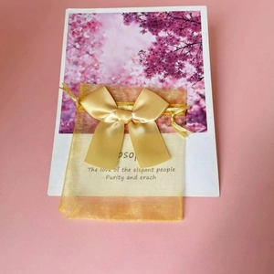Detail of a golden organza gift bag with a sleek satin ribbon bow on floral card