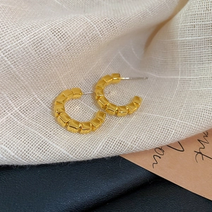 Detailed close-up of golden geometric C-shaped earrings with cube texture on textured fabric