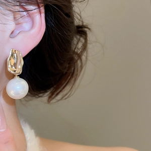 Detail of round white pearl earrings with irregular golden hammered metal texture