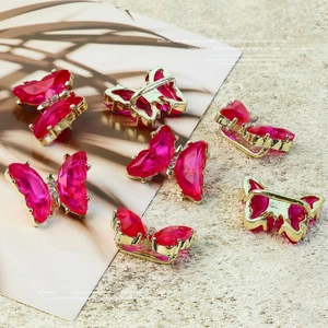 Detailed view of luxury red crystal butterfly nail charms with gold diamond-encrusted edges